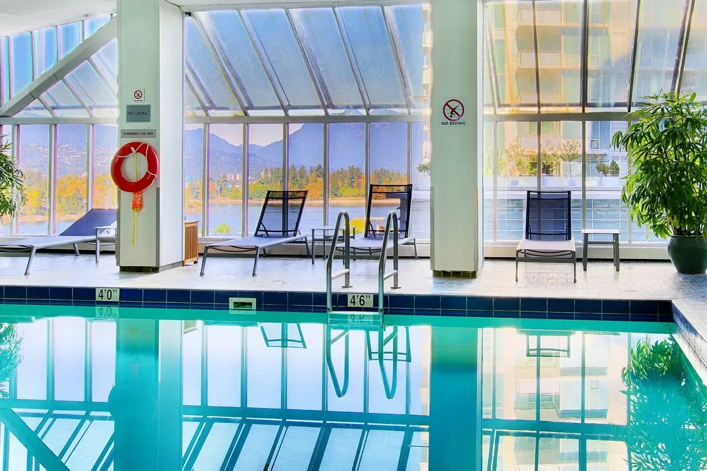 A covered indoor pool terrace with loungers, looking out across the water and mountains from Vancouver, British Columbia